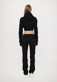 Melnā īsā kapuce ar kapuci, apvienota ar šauriem melniem džinsiem. Mīksta tekstūra un minimālistisks dizains, baltas sporta apavi noslēdz apģērbu.