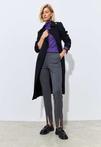 Black trench coat, purple turtleneck, gray tailored pants with side slits, black loafers with chunky soles, smooth fabric textures.