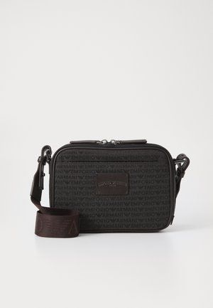 Bolsa de ombro em tecido preto com padrão de logótipos repetido, fecho com zíper e alça ajustável com detalhe do logótipo. Textura lisa, formato retangular.