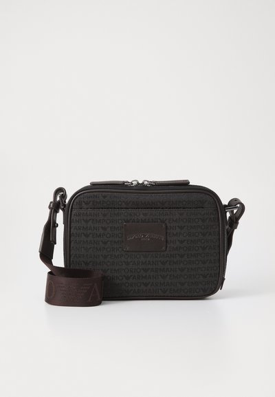 Czarna torebka crossbody z tkaniny, z powtarzającym się wzorem logo, zamkiem błyskawicznym oraz regulowanym paskiem z detalem logo. Gładka tekstura, prostokątny kształt.