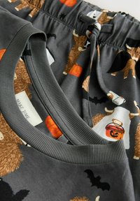 Grijze stof met speelse illustraties van koeien, pompoenen en vleermuizen, voorzien van een elastische tailleband en trekkoord.