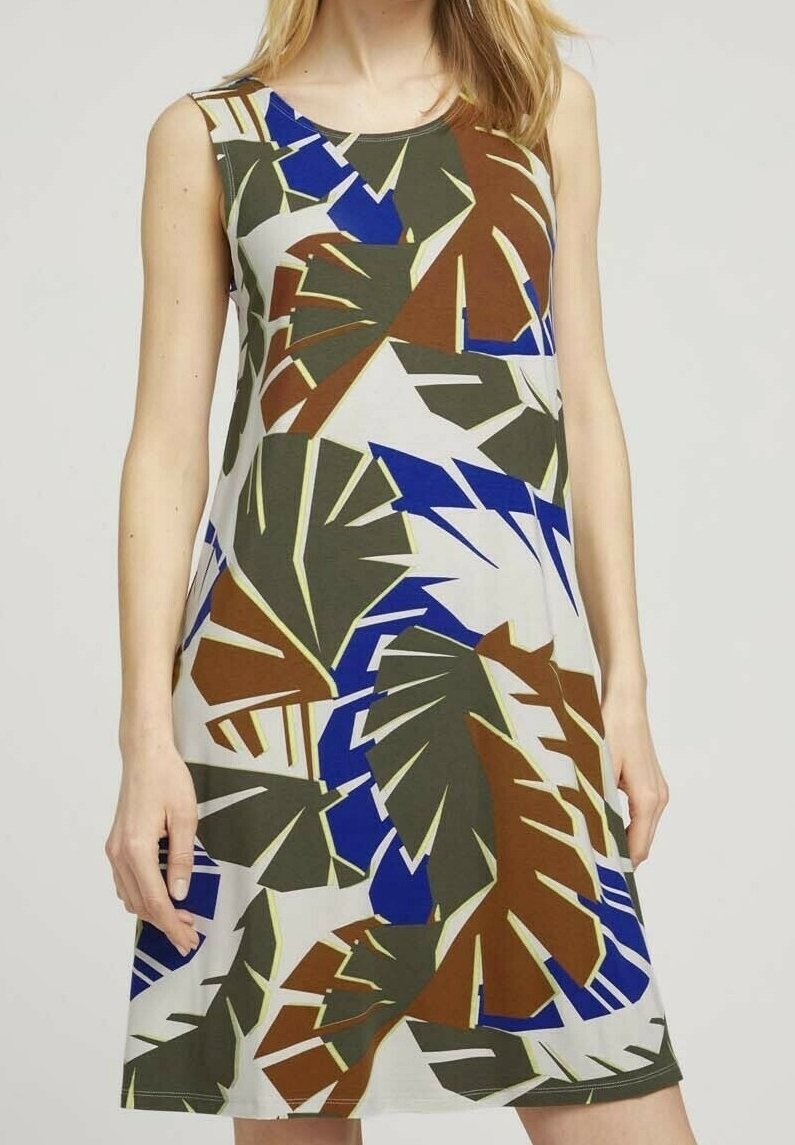 Robe sans manches avec un grand imprimé abstrait de feuilles en marron, vert, bleu et blanc portée par une personne debout sur un fond uni.