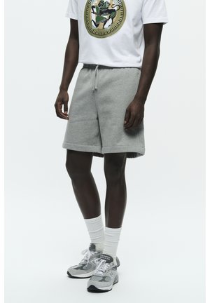 Grey fleece shorts with an elastic waistband, side pockets, and a relaxed fit. Paired with a white graphic t-shirt and grey sneakers.
