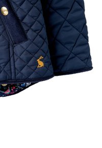 Chaqueta acolchada navy con bordado de conejo dorado, con un forro interior floral y un borde texturizado a lo largo del dobladillo y el bolsillo.
