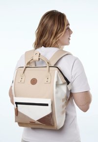 Beige-weißer Rucksack mit geometrischem Design, Lederelementen, verstellbaren Trägern, einer vorderen Reißverschlusstasche und einem runden Logopatch.