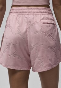 Primer plano de una persona que lleva pantalones cortos de rizo rosa con una cinturilla elástica y un patrón de texto en cursiva en relieve.