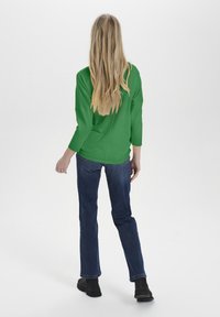 Zielony prążkowany sweter z rękawami do łokcia, zestawiony z niebieskimi dżinsami i czarnymi botkami, widziany od tyłu.