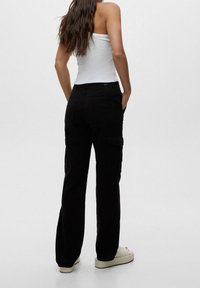 Pantalons cargo noirs avec poches latérales, fabriqués en coton. Le design présente une coupe décontractée et une jambe légèrement fuselée, associés à un débardeur blanc.