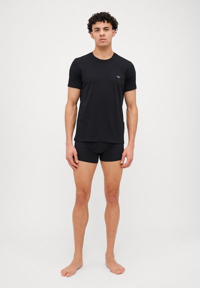 Tricou negru din bumbac cu mâneci scurte și guler rotund, asociat cu șorturi boxer negre. Design simplu, fără modele sau accesorii vizibile.