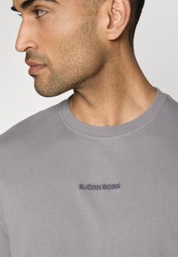 Tricou gri din bumbac, cu guler rotund. Prezintă un text brodat de culoare albastră închis "BJÖRN BORG" pe piept. Textură moale.
