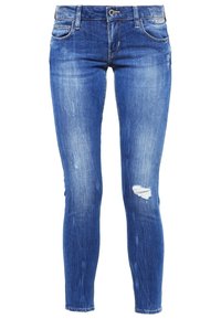 Jean skinny bleu avec un effet délavé, fermeture avant par bouton et zip, style classique à cinq poches, et une petite zone usée sur la cuisse droite.
