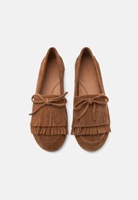 Καφέ σουέντ μοκασίνια με διακοσμητικές φούντες και δεμένα φιόγκους στην κορυφή, εμφανιζόμενα από πάνω σε λευκό φόντο.