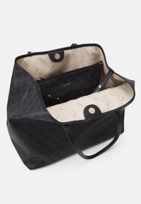 Zwarte getextureerde tote bag met dubbele handgrepen, gouden hardware en een beige interieur met groene logo-opdruk. Inclusief een ritsvak aan de binnenzijde.
