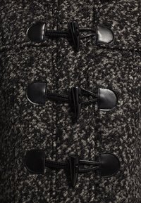 Czarny i szary wełniany płaszcz w melanż, z zapięciem na toggles; posiada gładkie akcenty z czarnej skóry oraz teksturowany, gruby wzór splotu.