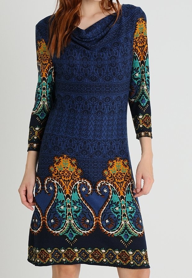 Femme portant une robe cintrée longueur genou avec manches longues, arborant un motif floral et géométrique complexe en bleu, orange, vert et noir.