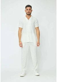 Chemise à manches courtes en lin blanc à boutons, assortie à un pantalon tapered. Texture lisse ; les deux articles présentent un motif tissé subtil.