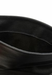 Zwarte leren tas met een zachte, gestructureerde buitenkant. Het interieur is glad, met een slank, open ontwerp en geen zichtbare hardware.