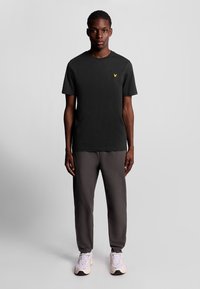 Svart t-Shirt med kort ärm och en liten gul logotyp, kombinerat med gråa sweatpants och ljusa sportskor.