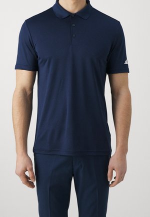 Homme portant un polo bleu marine à manches courtes avec une patte de boutonnage à trois boutons et un pantalon bleu marine assorti, debout devant un fond uni.