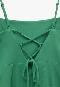 Top verde sin mangas con diseño de escote en V. Presenta tirantes entrecruzados y un detalle de lazo en la cintura. Tejido suave y con textura.