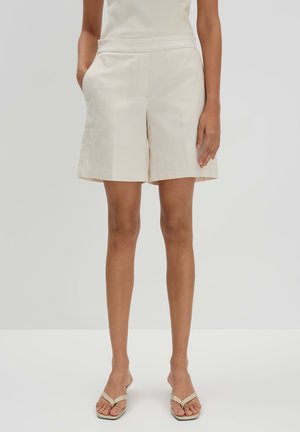 Beige katoenen shorts met een rechte voorkant, zijzakken en een relaxte pasvorm, tot boven de knie, gecombineerd met lichte slippers.