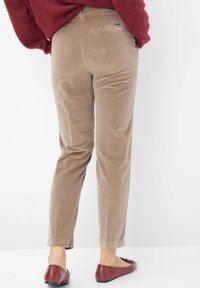 Beige corduroy broek met een slim fit, taps toelopende pijpen en achterzakken. De textuur is zacht met een lichte glans. G gedragen met bordeauxrode flats.