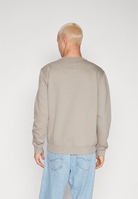Sweatshirt color beige chiaro con scollo a giro, polsini e orlo a costine, e un piccolo etichetta sul retro. Indossato con jeans blu chiaro.