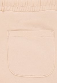 Tessuto beige chiaro con una texture liscia caratterizzato da una singola tasca applicata. La tasca ha angoli arrotondati e dettagli di cucitura visibili.