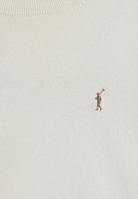 Tessuto a maglia color crema con piccolo logo ricamato marrone raffigurante una persona che porta una mazza da golf sulla spalla.