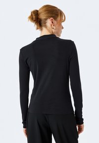 Czarny longsleeve wykonany z prążkowanej tkaniny, o dopasowanym kroju i okrągłym dekolcie. Bez widocznych wzorów i ozdób.