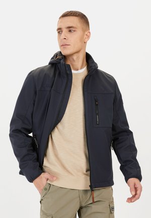 Marinejacke mit Kapuze, ausgestattete mit einer Reißverschluss-Brusttasche, Seitentaschen und einer glatten, matten Textur. Getragen über einem beigen Pullover.