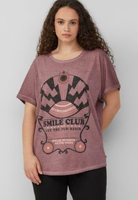 Lila Baumwoll-T-Shirt mit rundem Ausschnitt und kurzen Ärmeln, das einen grafischen Druck in schwarzer und oranger Schrift mit dekorativen Elementen zeigt.