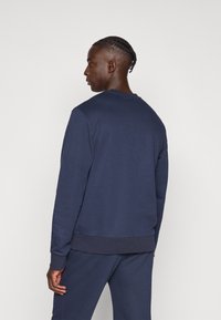 Μπλε σκούρα φούτερ με στρογγυλή λαιμόκοψη, μακριά μανίκια και ριμπ μανσέτες. Κατασκευασμένο από απαλό υλικό με άνετη εφαρμογή και μονόχρωμο σχέδιο.