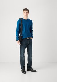 Cămașă albastră cu mâneci lungi, blugi negri și pantofi negri. Geantă crossbody neagră cu curea ajustabilă. Îmbrăcăminte simplă și casuală.