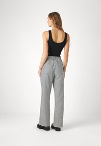 Schwarzes Tanktop und hoch taillierte, weite Hose mit schwarz-weißen vertikalen Streifen. Verfügt über Gesäßtaschen und strukturierte Stoffe.