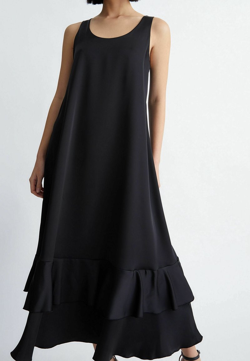 Robe noire sans manches en tissu lisse, dotée d'un ourlet évasé avec un détail de volants au bas, design minimaliste et coupe décontractée.