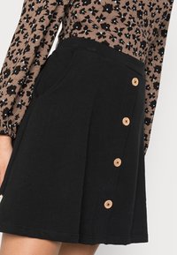 Saia preta de corte godê feita de um tecido suave, com uma fileira lateral de cinco botões de madeira e dois bolsos laterais.