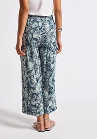 Wide-leg pants with a blue and white snake print pattern. Soft fabric, elastic waistband, and two back pockets. Paired with flat sandals.