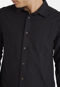 Black button-up shirt made of soft, textured fabric. Features a classic collar, front buttons, and long sleeves.