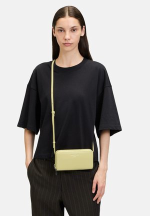 Crossbody-Tasche aus hellgelbem Leder, rechteckige Form, glatte Oberfläche, ausgestattet mit einem dünnen verstellbaren Schulterriemen und einem Reißverschluss.