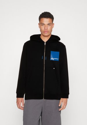 Felpa nera con zip e una toppa blu con la scritta "Karl Lagerfeld Jeans." Include un cappuccio e una tasca frontale, realizzata in tessuto di cotone.