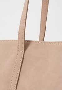 Beige Kunstleder-Shopper mit zwei vertikalen Griffen, sichtbaren Nähten und einer glatten Textur. Schlichtes Design ohne zusätzliche Muster.