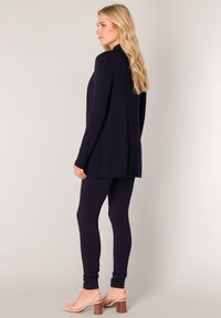 Marineblauwe cardigan met lange mouwen, gecombineerd met bijpassende leggings, gemaakt van zachte stof. Open voorkant ontwerp, minimalistisch zonder zichtbare patronen.