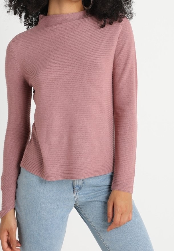 Top rosa a maniche lunghe con texture a coste e collo alto, abbinato a jeans azzurri. Tessuto morbido e vestibilità comoda.