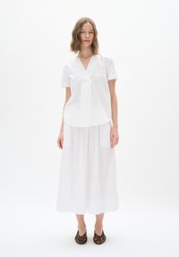 White short-sleeve blouse with a V-neck, featuring a pleated design. Paired with a flowing white skirt and leopard-print flats.