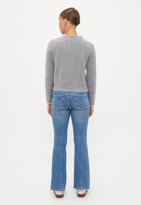 Γκρι πλεχτό πουλόβερ με στρογγυλή λαιμόκοψη και ριμπ τελείωμα, συνδυασμένο με ανοιχτό μπλε καμπάνα τζιν με πίσω τσέπες και ξεθωριασμένη όψη.