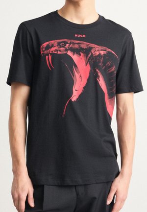 Man wearing black T-shirt with large red snake head graphic and "HUGO" text above the design on the chest.