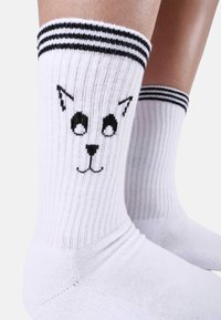 Vita strumpor med ribbad textur, svart kattansiktsmotiv och kontrasterande svartvita ränder högst upp.