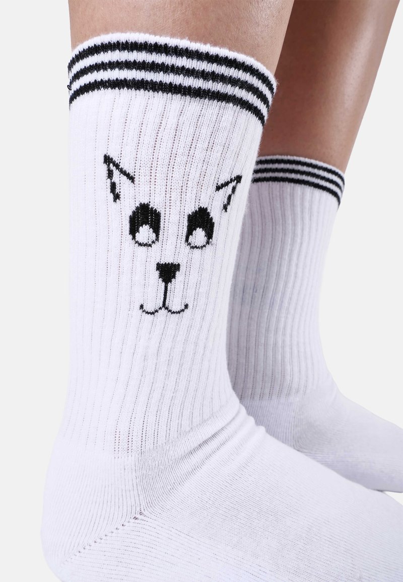 Vita strumpor med ribbad textur, svart kattansiktsmotiv och kontrasterande svartvita ränder högst upp.