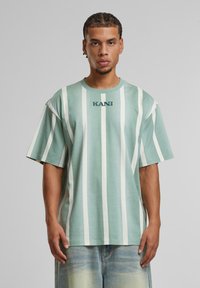 Mintgrønn t-skjorte med hvite vertikale striper, korte ermer og rund hals. Har "KANI"-logoen trykt på brystet i mørkeblå.
